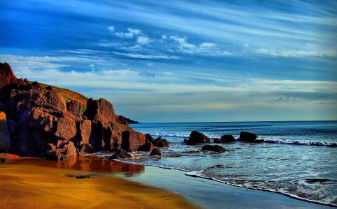 Strand, Klippen und Meer unter blauem Himmel