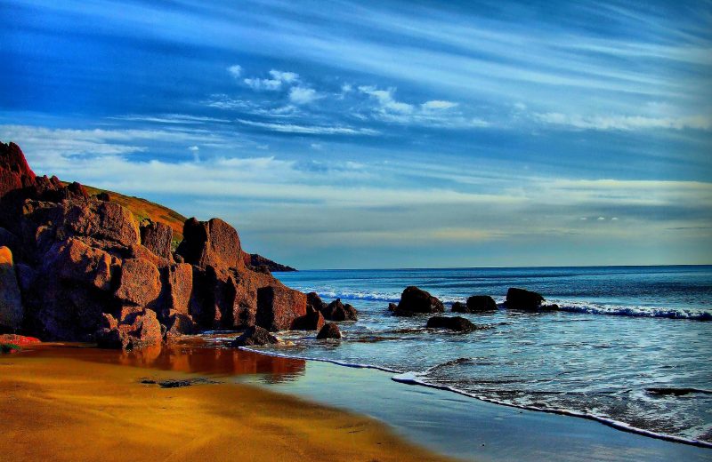 Strand, Klippen und Meer unter blauem Himmel