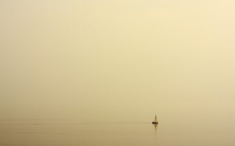 Ein kleines Segelboot am Horizont eines unüberschaubaren, nebligen Meers